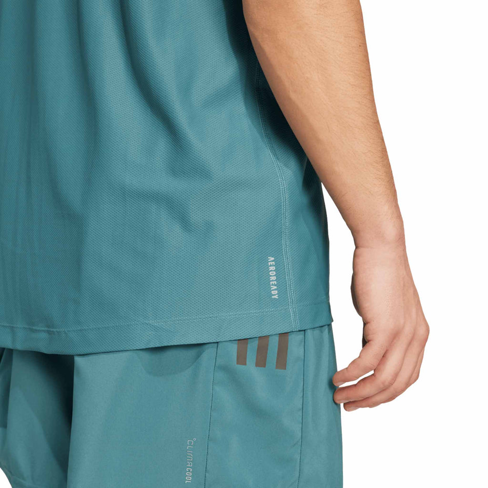 Close up of the AEROREADY branding on the bottom, back right of the adidas Men's Own The Run Base Tee in the Preloved Teal colourway. (8663053500578)