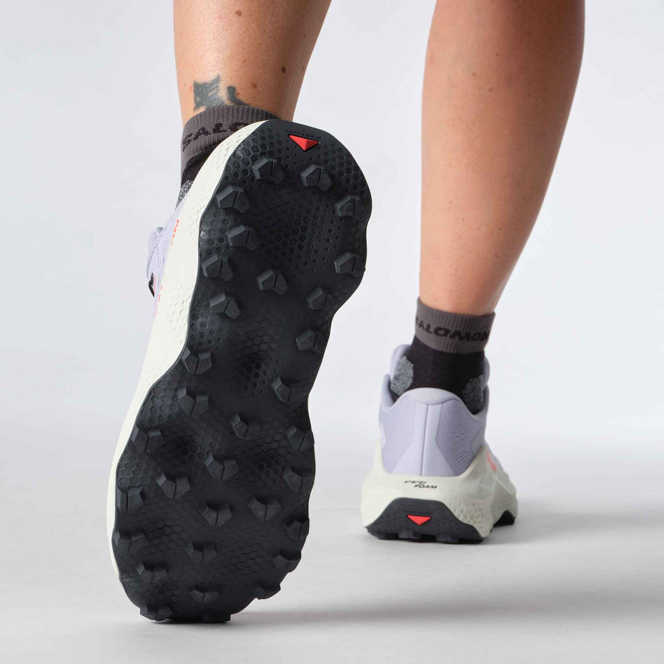 A model showing off the grip on the left shoe from a pair of Salomon Women's Ultra Glide 3 Running Shoes in the Cosmic Sky/Icicle/Neon Flame colourway. (8576019497122)