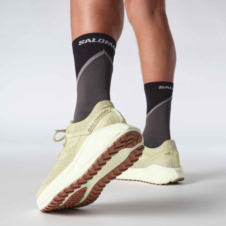 Angled view of a model wearing a pair of Salomon Men's Aero Glide 3 GRVL Running Shoes in the Green Haze/Vanilla Ice/Russet colourway. (8783469805730)