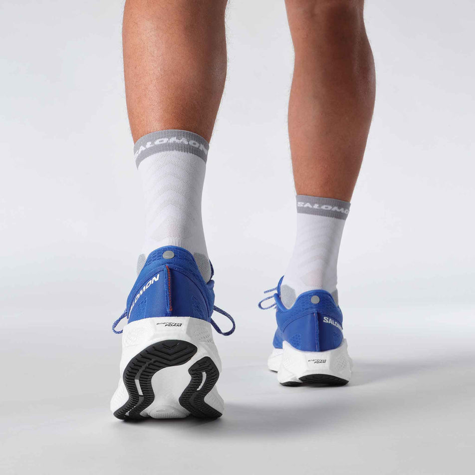 The back of a model wearing a pair of Salomon Men's Aero Glide 3 Running Shoes in the French Blue/White/Cherry Tomato colourway. (8576008257698)