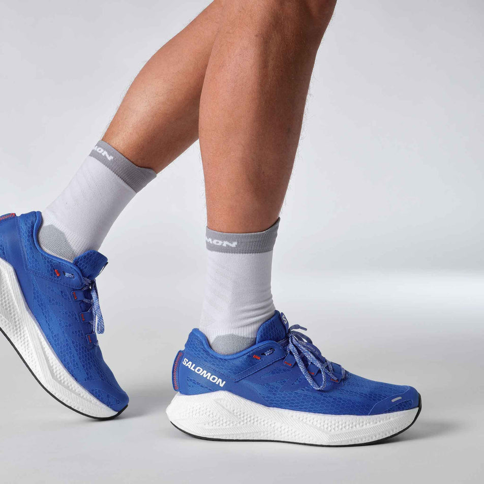 A model wearing a pair of Salomon Men's Aero Glide 3 Running Shoes in the French Blue/White/Cherry Tomato colourway. (8576008257698)