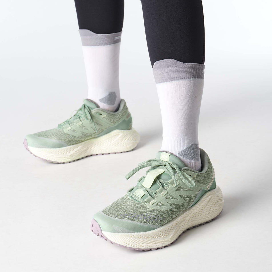 A model wearing a pair of Salomon Women's Aero Glide 3 GRVL Running Shoes in the Sea Foam/Vanilla Ice/Nirvana colourway. (8783556608162)