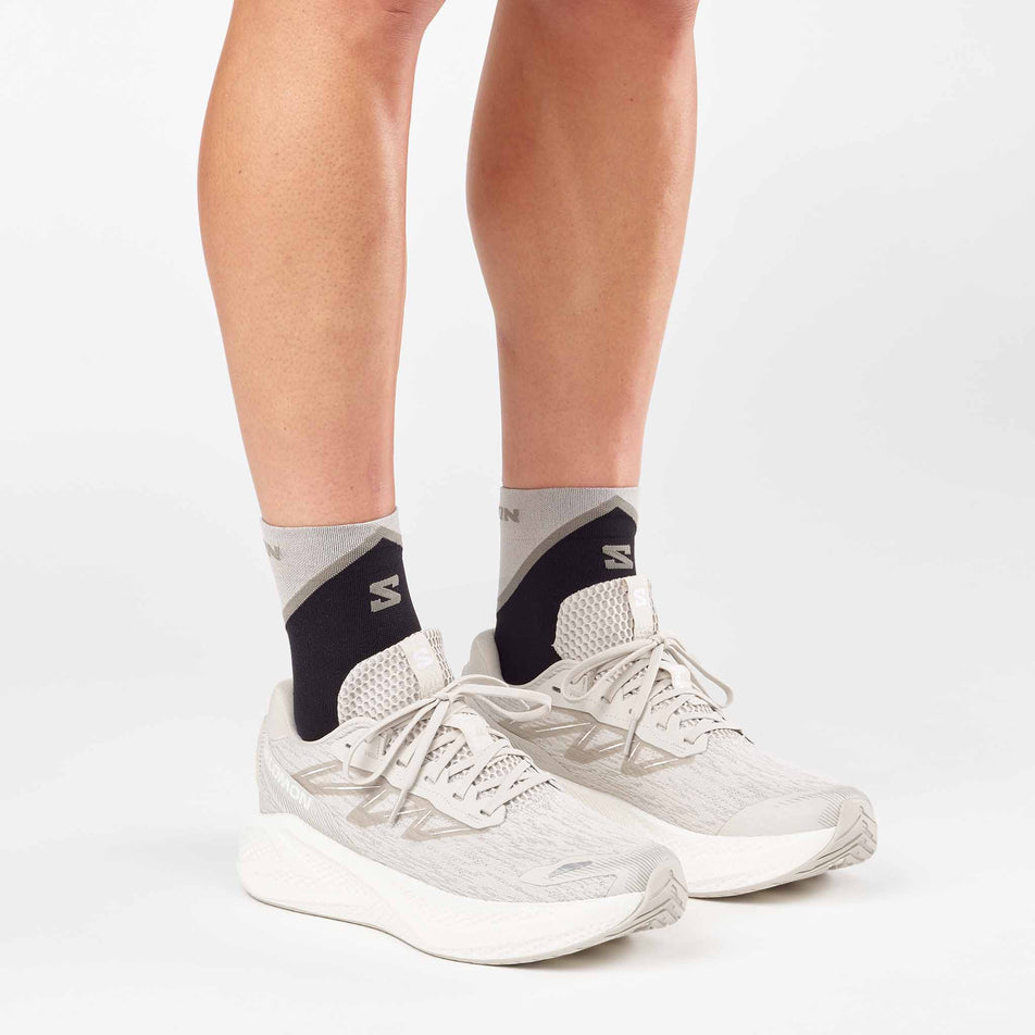 A model wearing a pair of Salomon Men's Aero Glide 4 Running Shoes in Silver Cloud/Silver Cloud/White colourway.