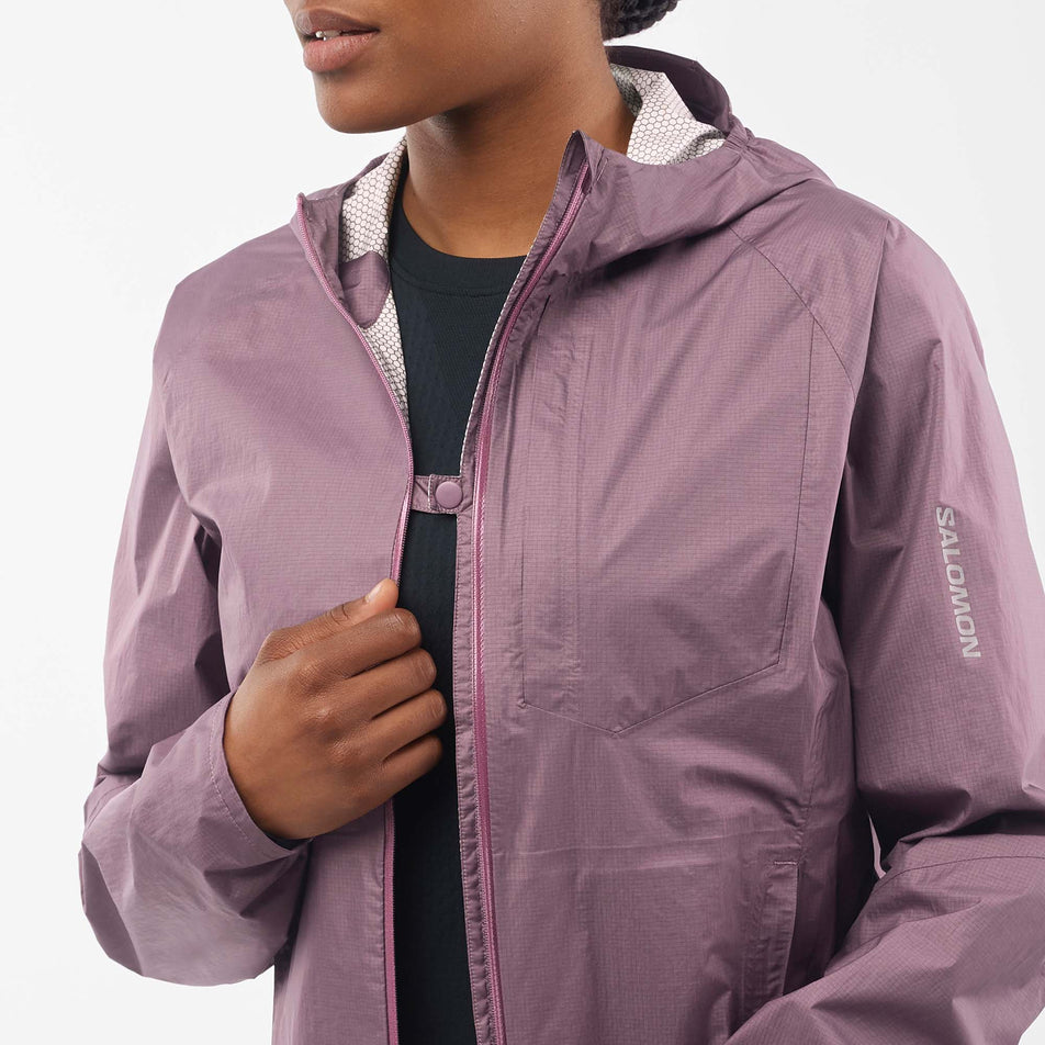 A model wearing a Salomon Women's Bonatti Waterproof Jacket in the Moonscape colourway, and demonstrating that the jacket can be clipped shut at the chest when it is unzipped.  (7999026266274)