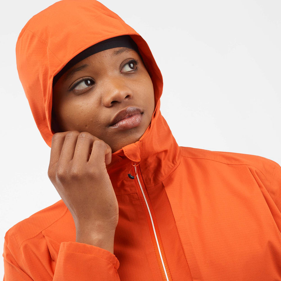 Close-up front view of a model wearing a Salomon Women's Bonatti Trail Jacket in the Burnt Ochre colourway, with the hood up. Upper part of the jacket is visible.  (8000727351458)