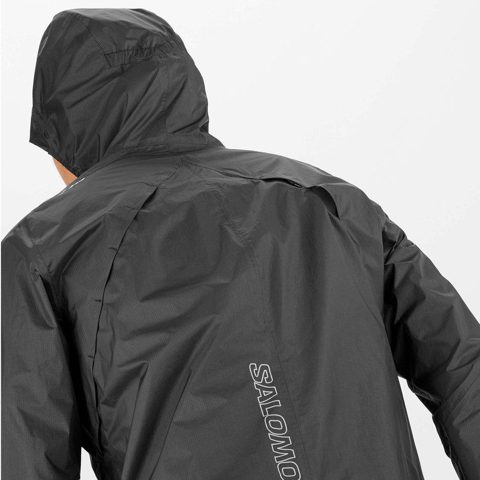 Close-up back view of a Salomon Men's Bonatti Waterproof Shell Jacket in the Deep Black colourway. Jacket is being worn by a model, with the hood up. (8466578342050)