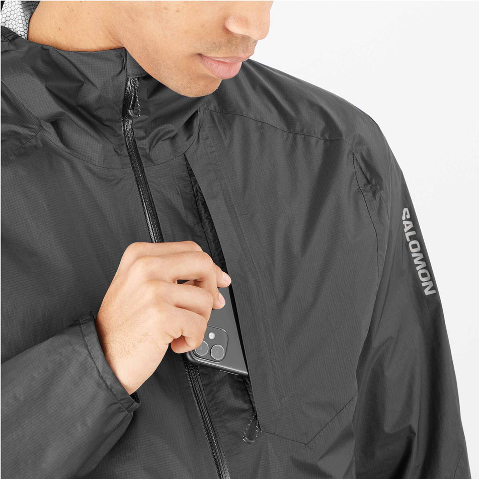 A model demonstrating that a phone can be stored in the chest pocket of a Salomon Men's Bonatti Waterproof Shell Jacket. Jacket is being worn by a model. (8466578342050)