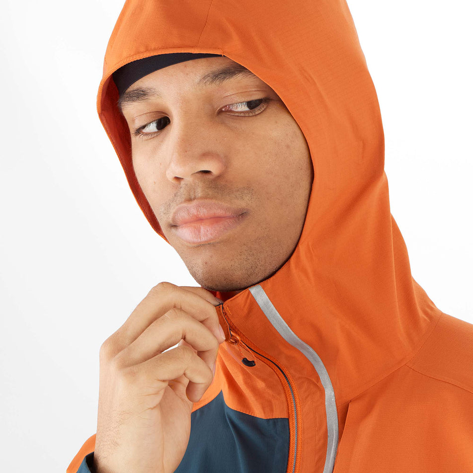Close-up front view of a model wearing a Salomon Men's Bonatti Trail Jacket in the Burnt Ochre/Carbon colourway, with the hood up. Only the upper part of the jacket is visible. (8008561098914)