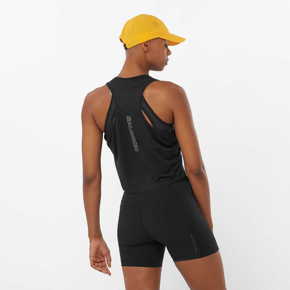 Back view of a model wearing a Salomon Women's Aero Short Tank in the Deep Black colourway. Model is also wearing shorts and a cap. (8311894966434)