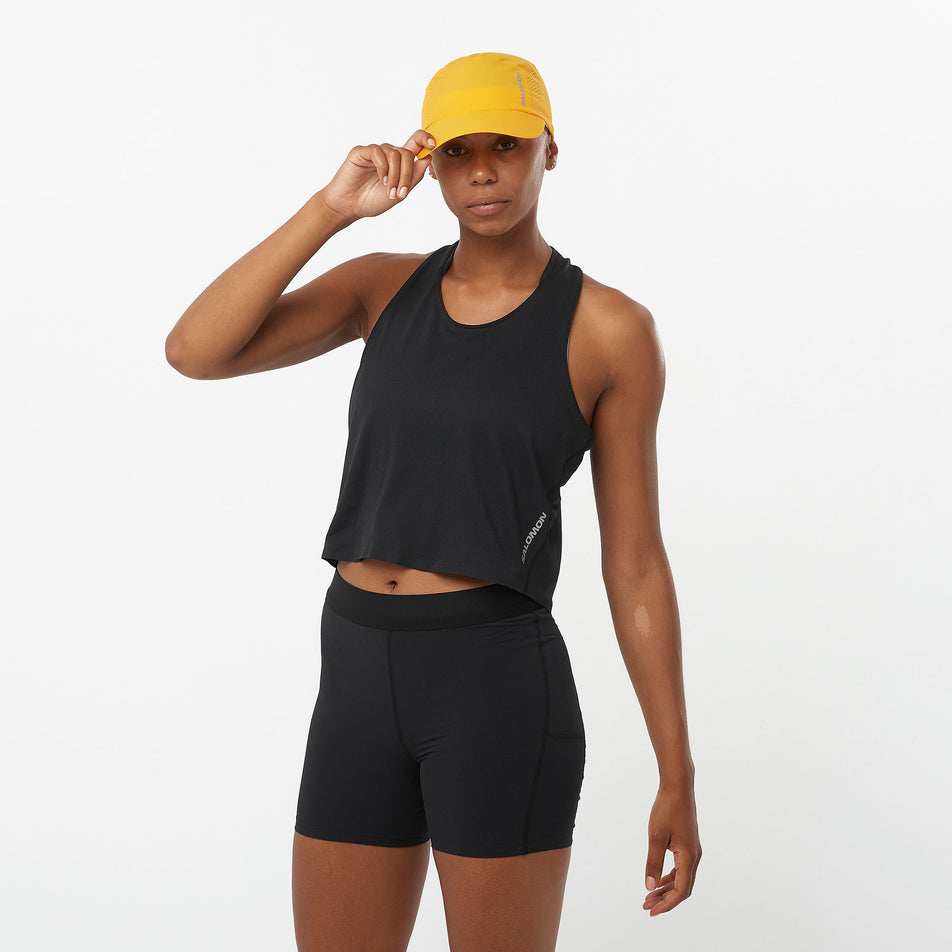 Front view of a model wearing a Salomon Women's Aero Short Tank in the Deep Black colourway. Model is also wearing shorts and a cap. (8311894966434)