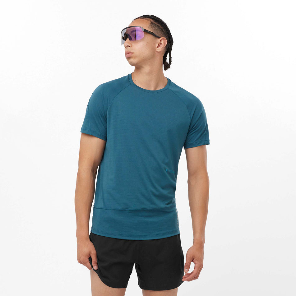 Front view of a model wearing a Salomon Men's Cross Run GFX Short Sleeve T-Shirt in the Deep Dive colourway. Model is also wearing shorts and sunglasses. (8157850534050)
