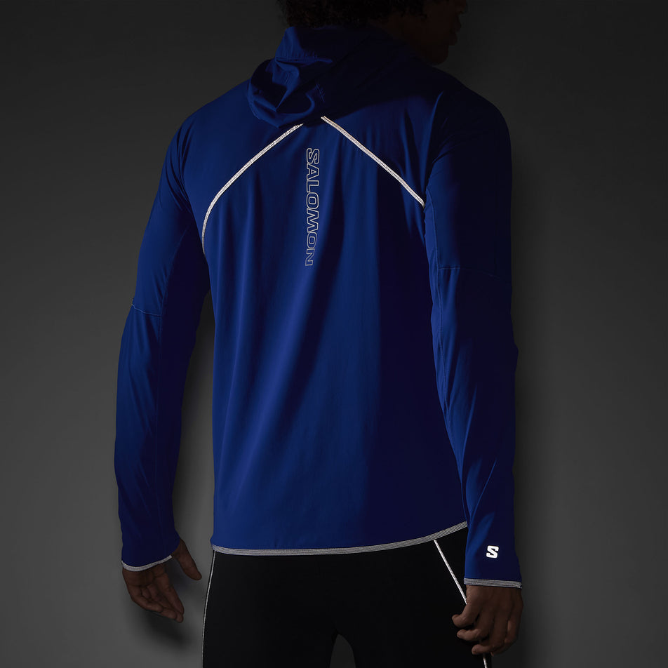 The reflectivity on the back of a Salomon Men's Sense Aero Hybrid Midlayer Jacket with hood in the Surf The Web colourway. Jacket is being worn by a model. (8464251617442)