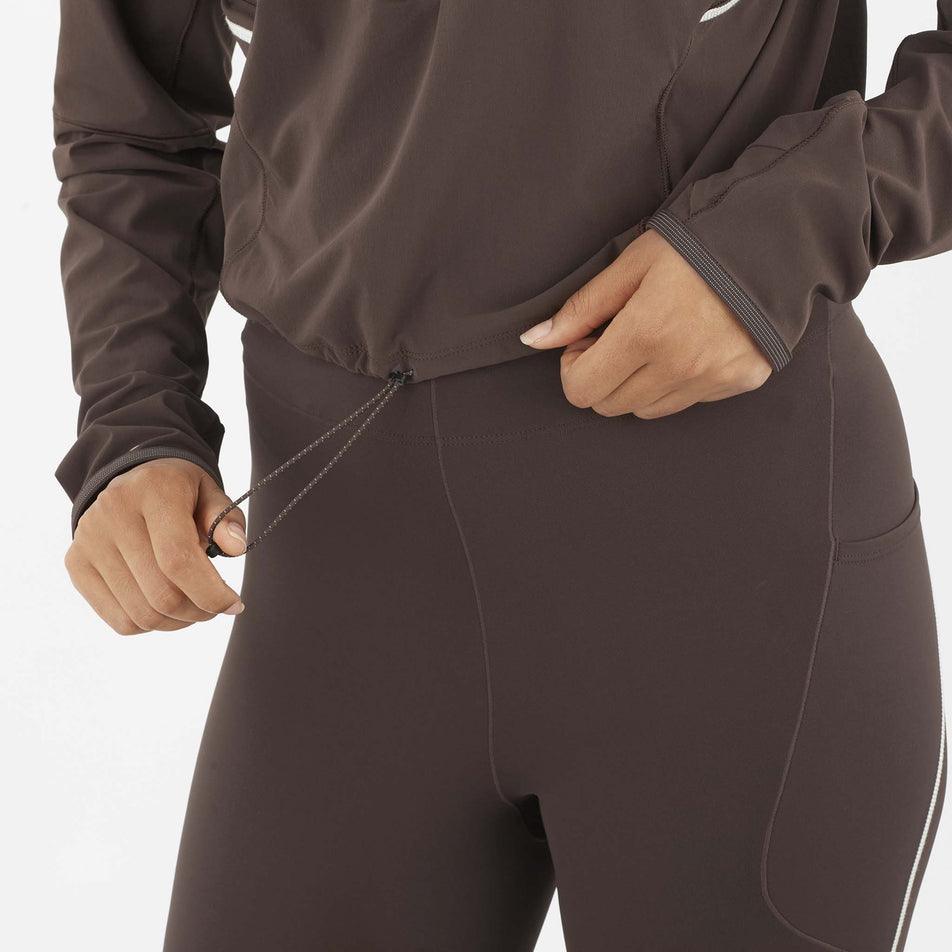A model demonstrating the waist cord on the Salomon Women's Sense Aero Hybrid Cropped Half Zip Midlayer in the Coffee Bean colourway. (8577396867234)