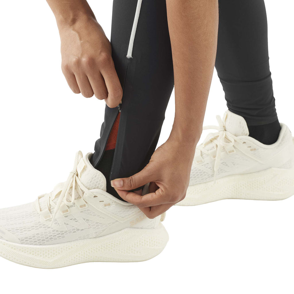 A model demonstrating the ankle zips on the Salomon Women's Sense Aero Stow Tights in the Deep Black colourway. (8727044685986)