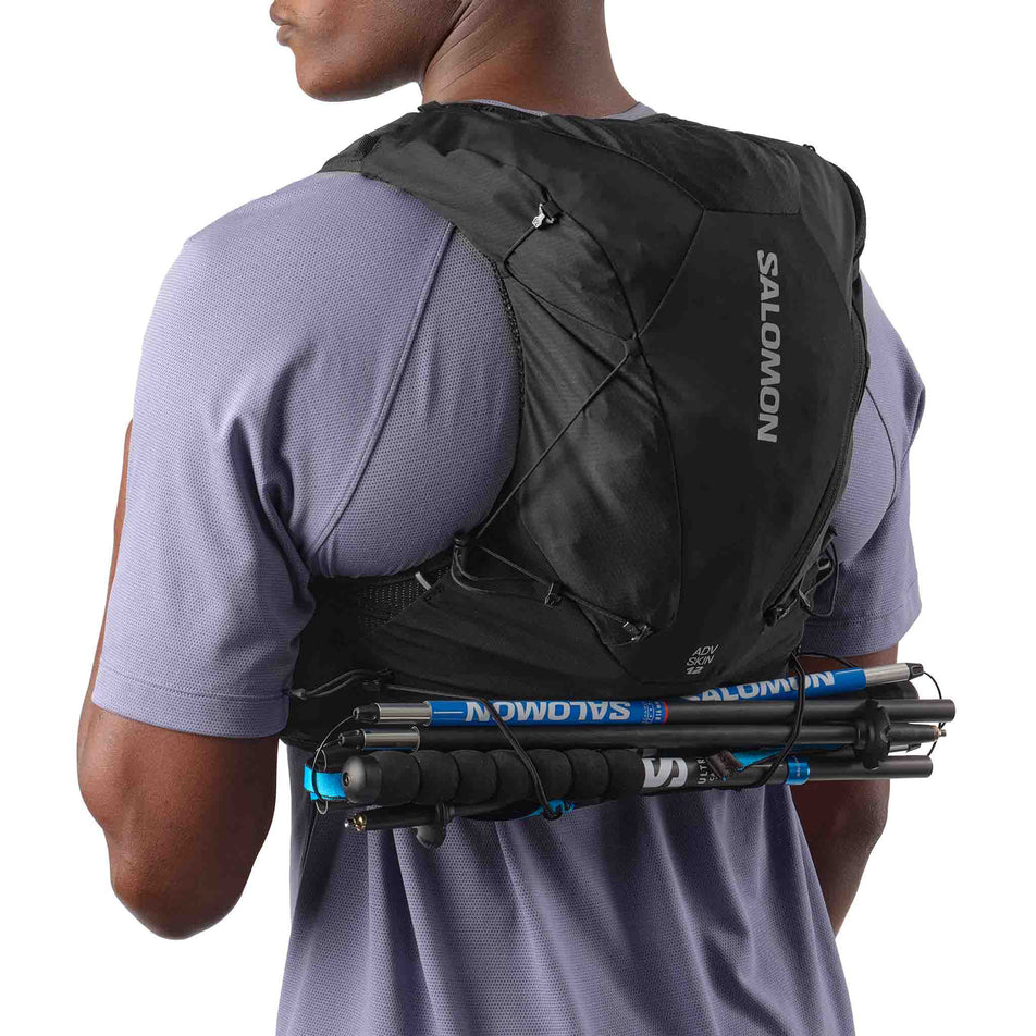 A model demonstrating running poles stowed in the Salomon Unisex ADV Skin 12 Running Vest in the Black colourway.