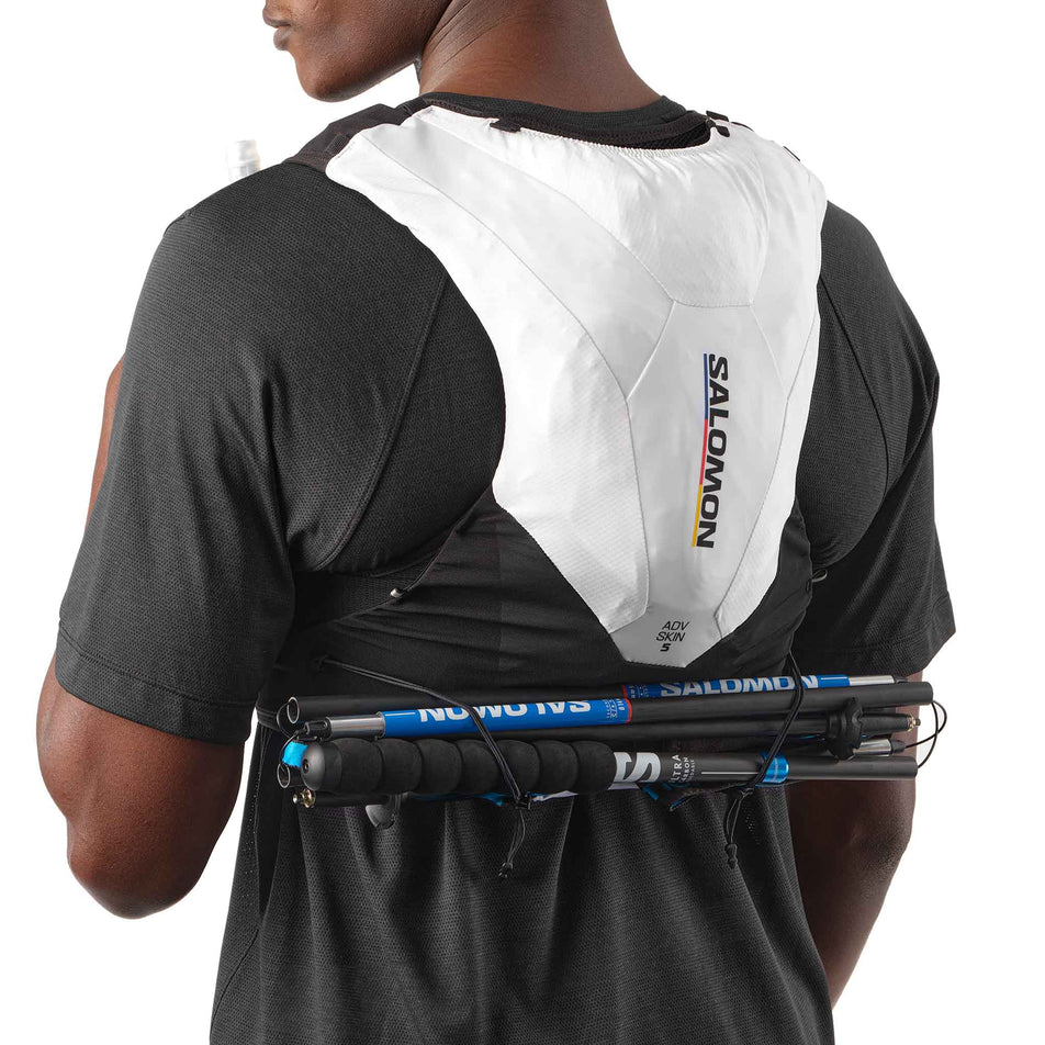 A model demonstrating the pole carrying capacity of the Salomon Unisex ADV Skin 5 Race Flag Running Vest with flasks included in the Black/White colourway. (8575896682658)
