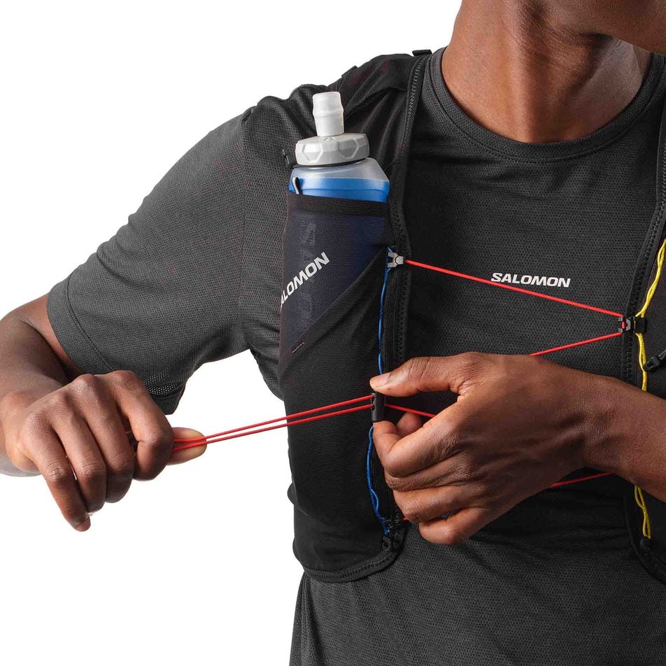 A model demonstrating the fastening system on the front of the Salomon Unisex ADV Skin 5 Race Flag Running Vest with flasks included in the Black/White colourway. (8575896682658)