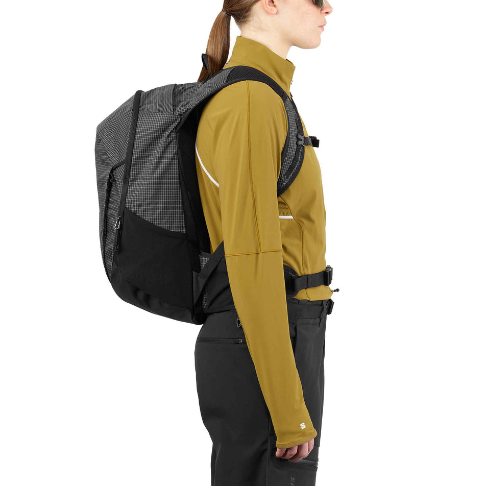 Side view of a model wearing the Salomon Unisex Trailblazer 20 Commuter Bag in the Black/White colourway. (8737342095522)