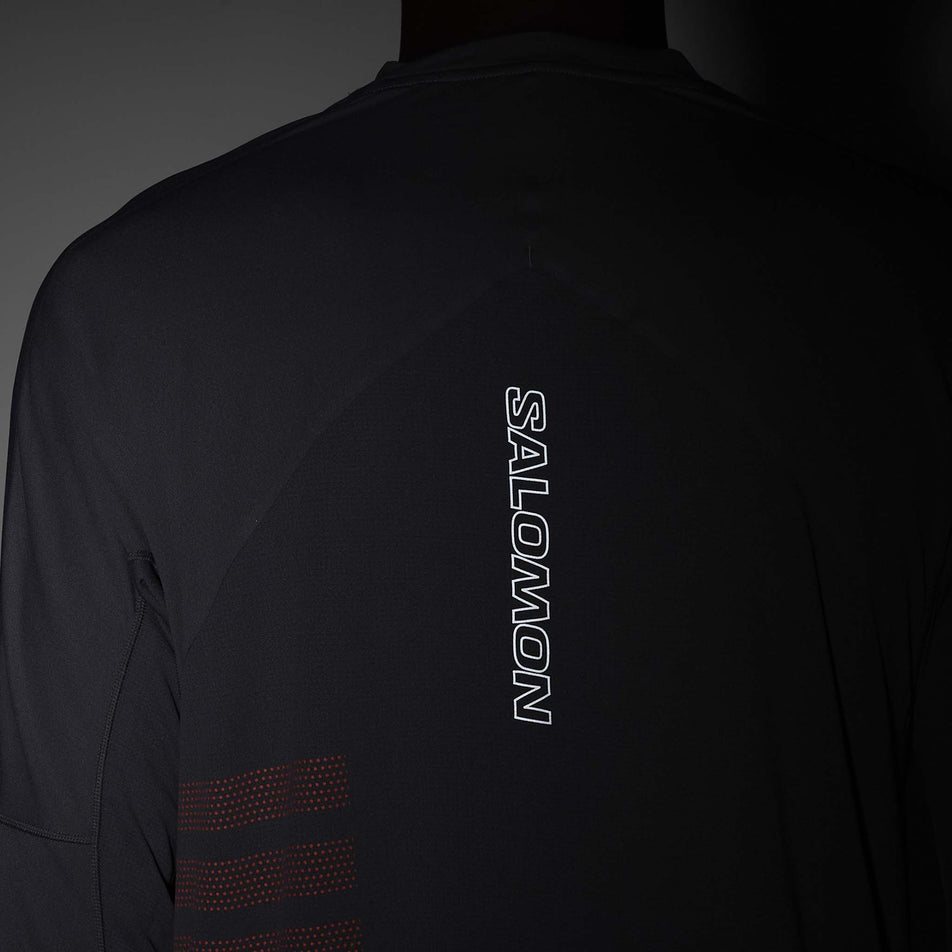 The reflective Salomon graphic on the back of the Salomon Men's Sense Aero Graphic Long Sleeve T-Shirt in the Castlerock/Neon Flame colourway. (8577952907426)