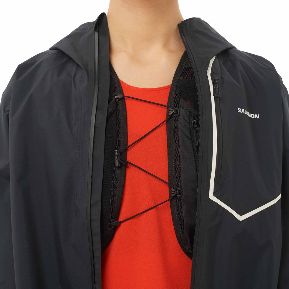 The Salomon Women's Bonatti Pro Shell Jacket in the Deep Black colourway worn over the top of a Salomon Hydration Vest.