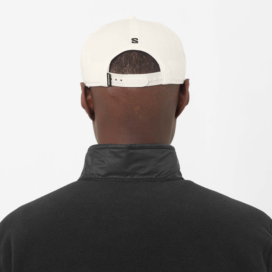 Back view of a model wearing the Salomon Unisex Logo Flat Cap in the Whisper White colourway.