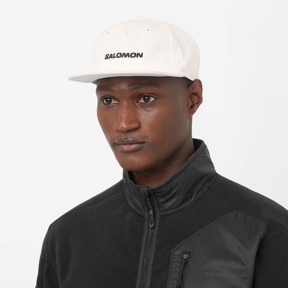Front view of a model wearing the Salomon Unisex Logo Flat Cap in the Whisper White colourway.