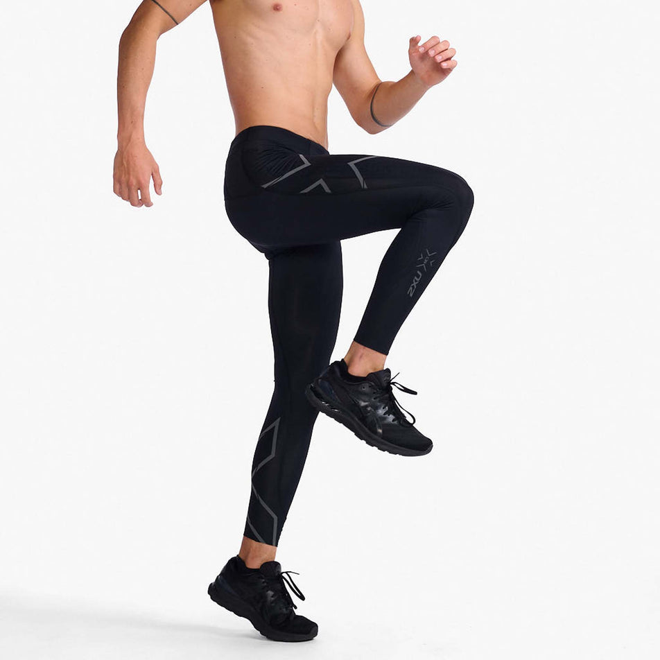 Side view of a model wearing a pair of 2XU Men's Light Speed Compression Tights in the Black/Black Reflective colourway. Model is in a running pose and wearing running shoes too. (8108325437602)