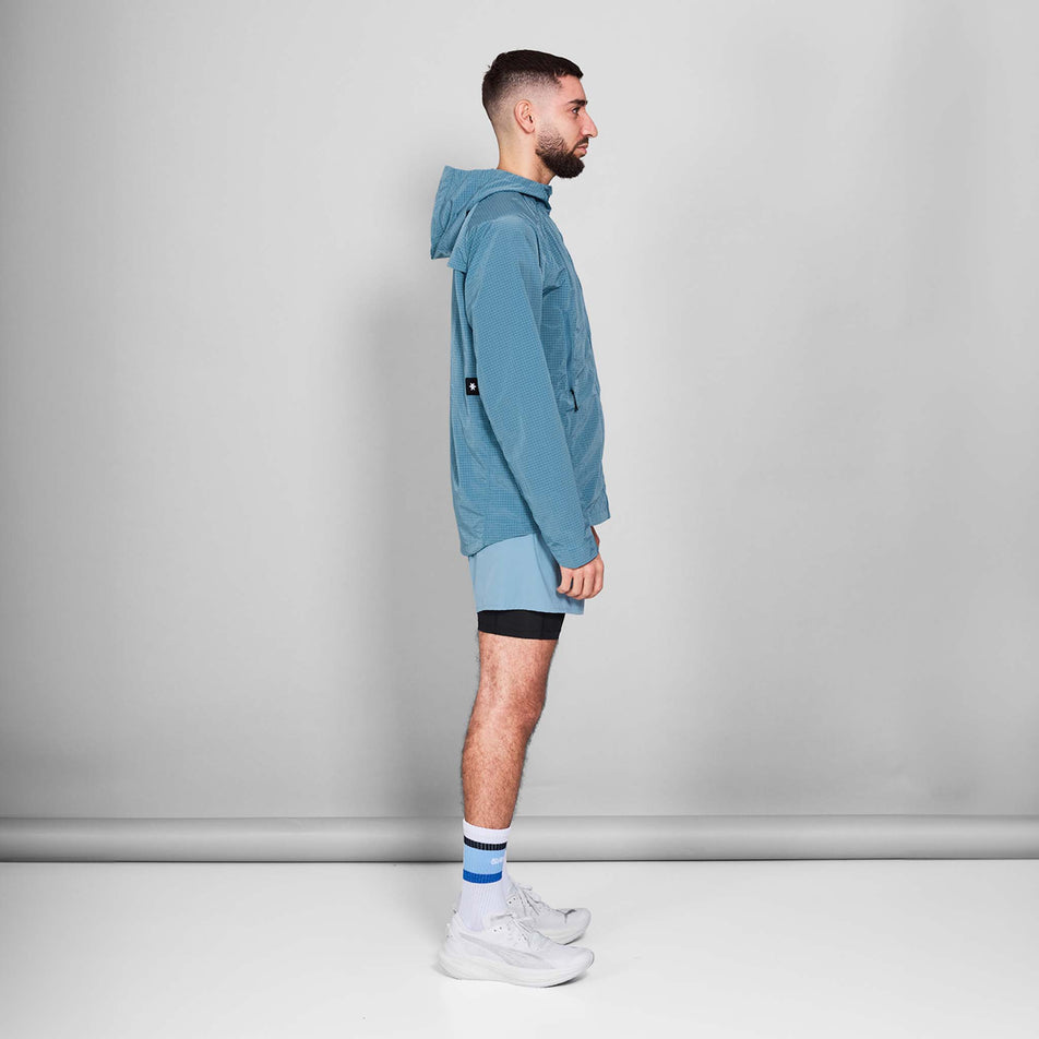 Side view of a model wearing the SAYSKY Men's Clean Pace Shield Jacket in the Blue colourway. Model is also wearing shoes, socks and shorts. (8601240633506)