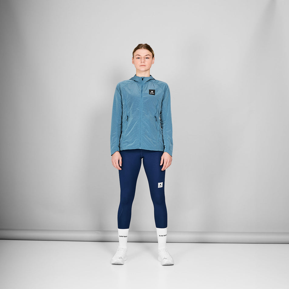Front view of a model wearing the SAYSKY Women's Clean Pace Shield Jacket in the Blue colourway. Model is also wearing tights, socks and shoes. (8601993445538)