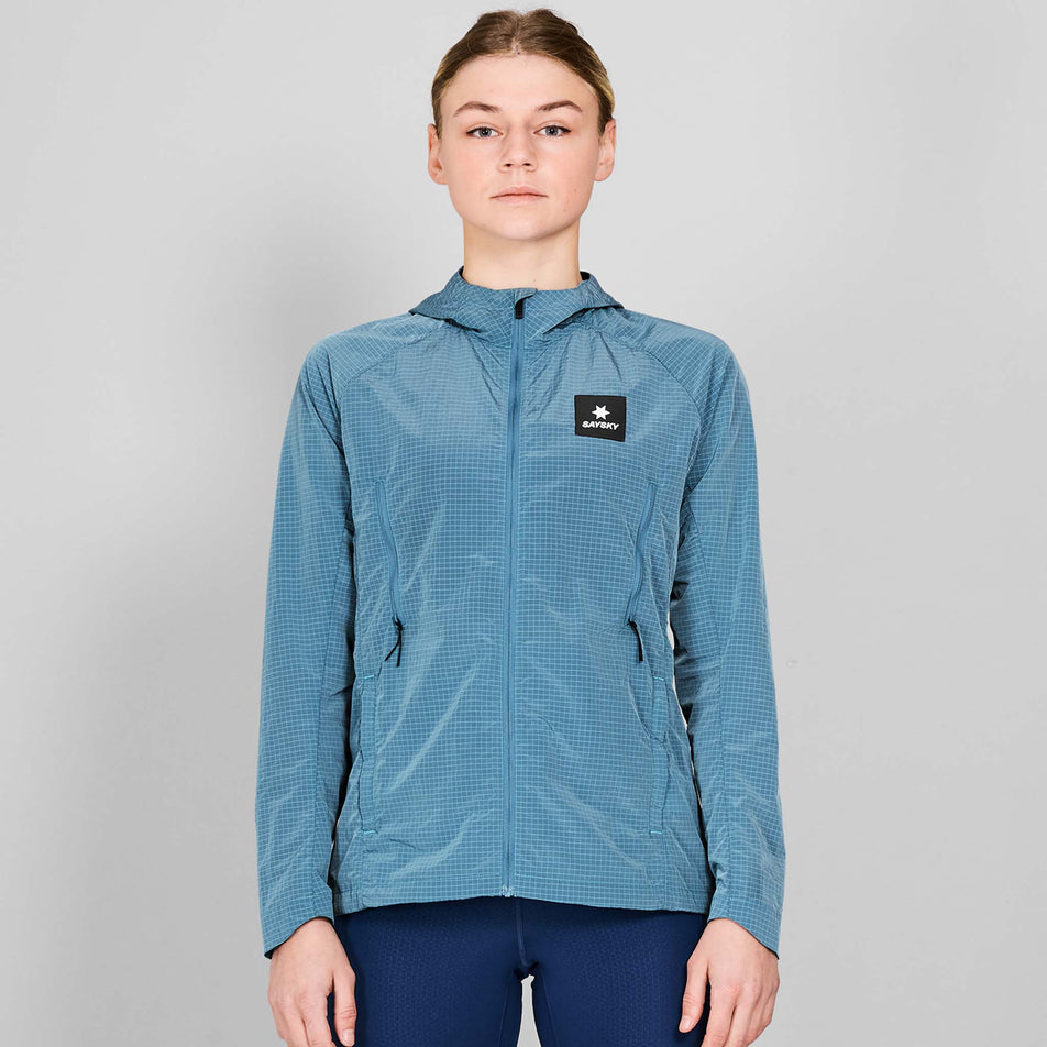 Front view of a model wearing the SAYSKY Women's Clean Pace Shield Jacket in the Blue colourway. Model is also wearing tights. (8601993445538)
