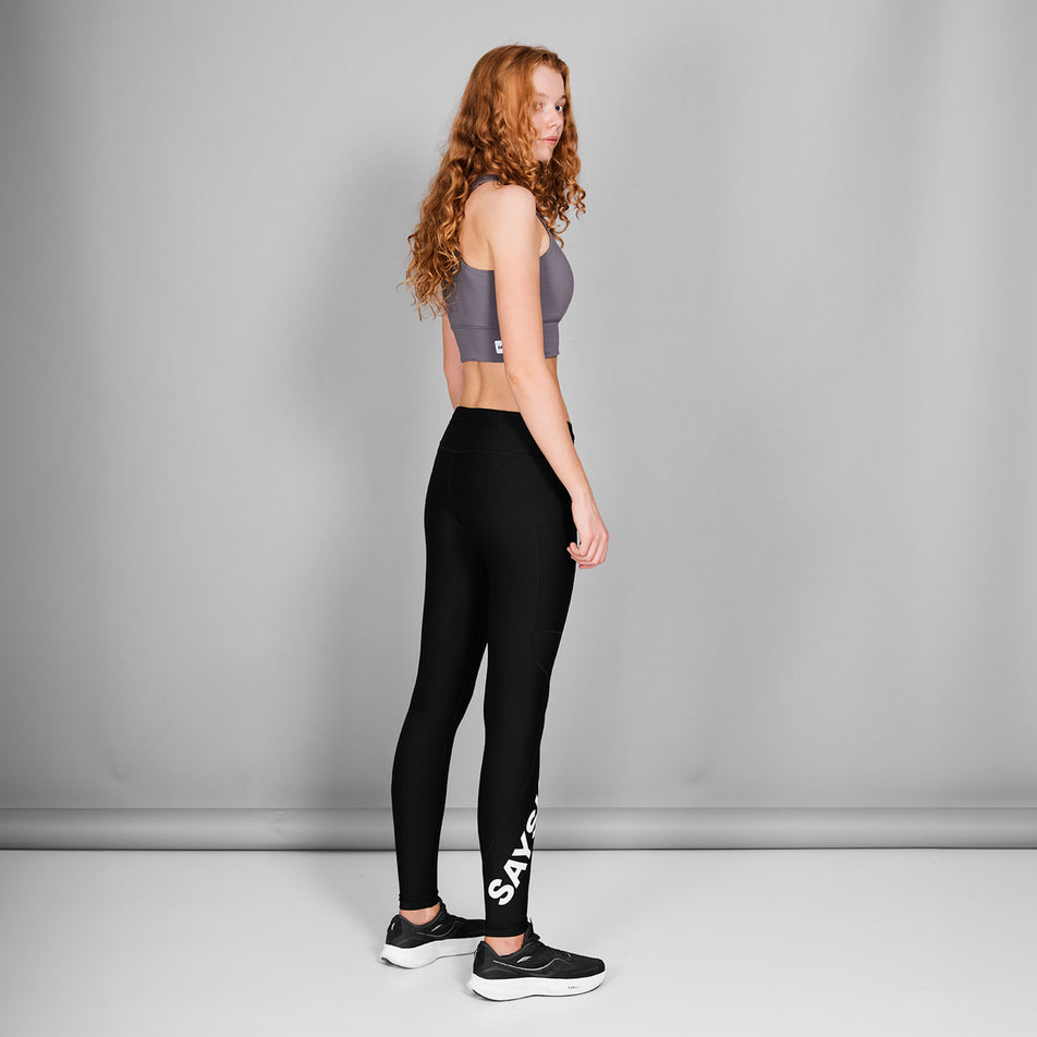 Back view of a model wearing the SAYSKY Women's Logo Motion+ Long Tights in the Black colourway. Model is also wearing shoes and a top. (8602027950242)