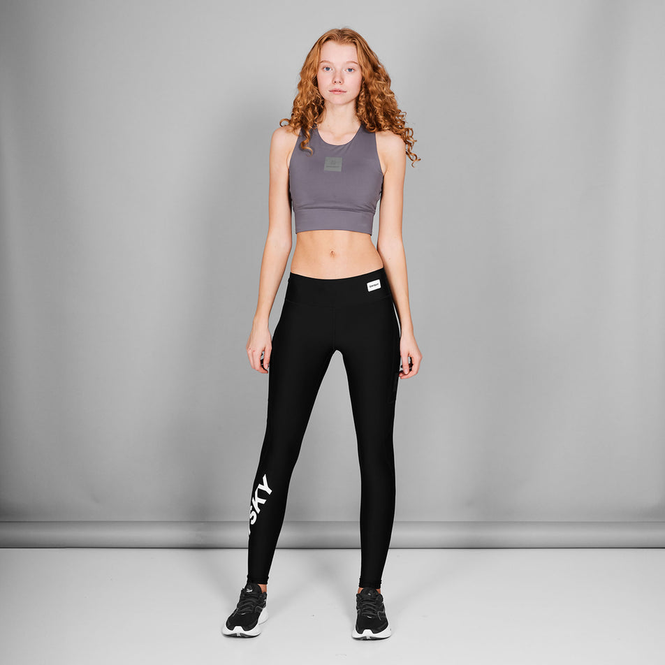 Front view of a model wearing the SAYSKY Women's Logo Motion+ Long Tights in the Black colourway. Model is also wearing shoes and a top. (8602027950242)