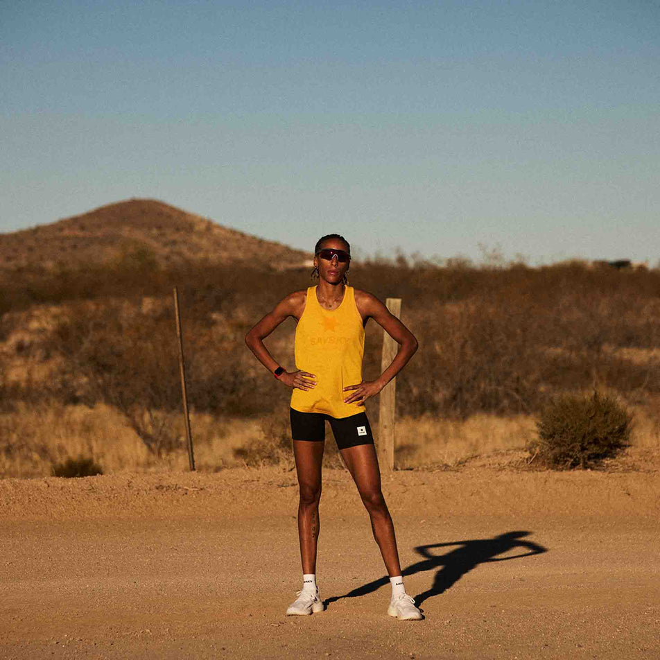 Front view of a model wearing the SAYSKY Women's Logo Combat Pro Singlet in the Yellow colourway. Model is also wearing shorts, socks and shoes. (8602088013986)