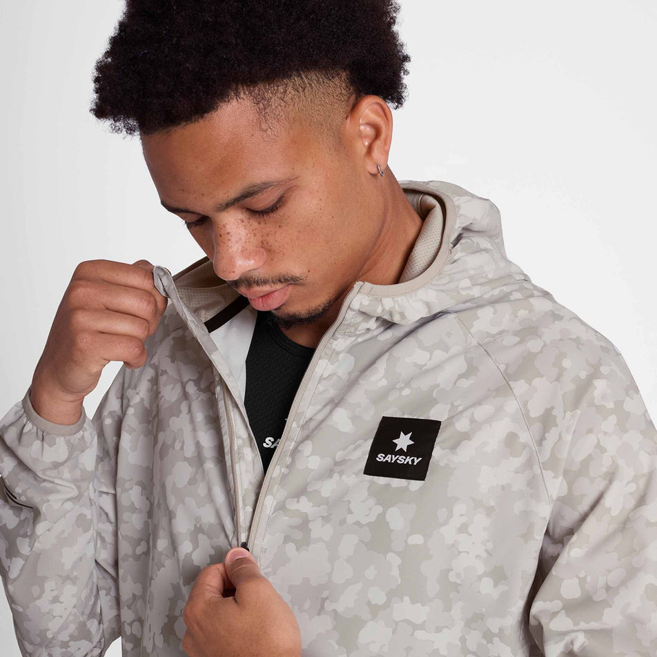A model adjusting the zip on the SAYSKY Men's Camo Pace Jacket in the White colourway. (8781019578530)
