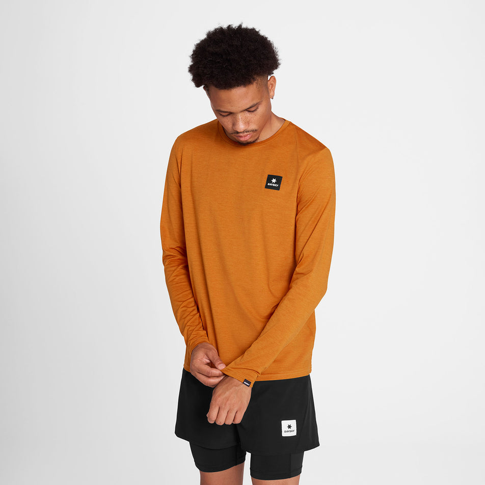 Front view of a model wearing the SAYSKY Men's Reflective Logo Pace Long Sleeve in the Orange colourway. (8788197605538)