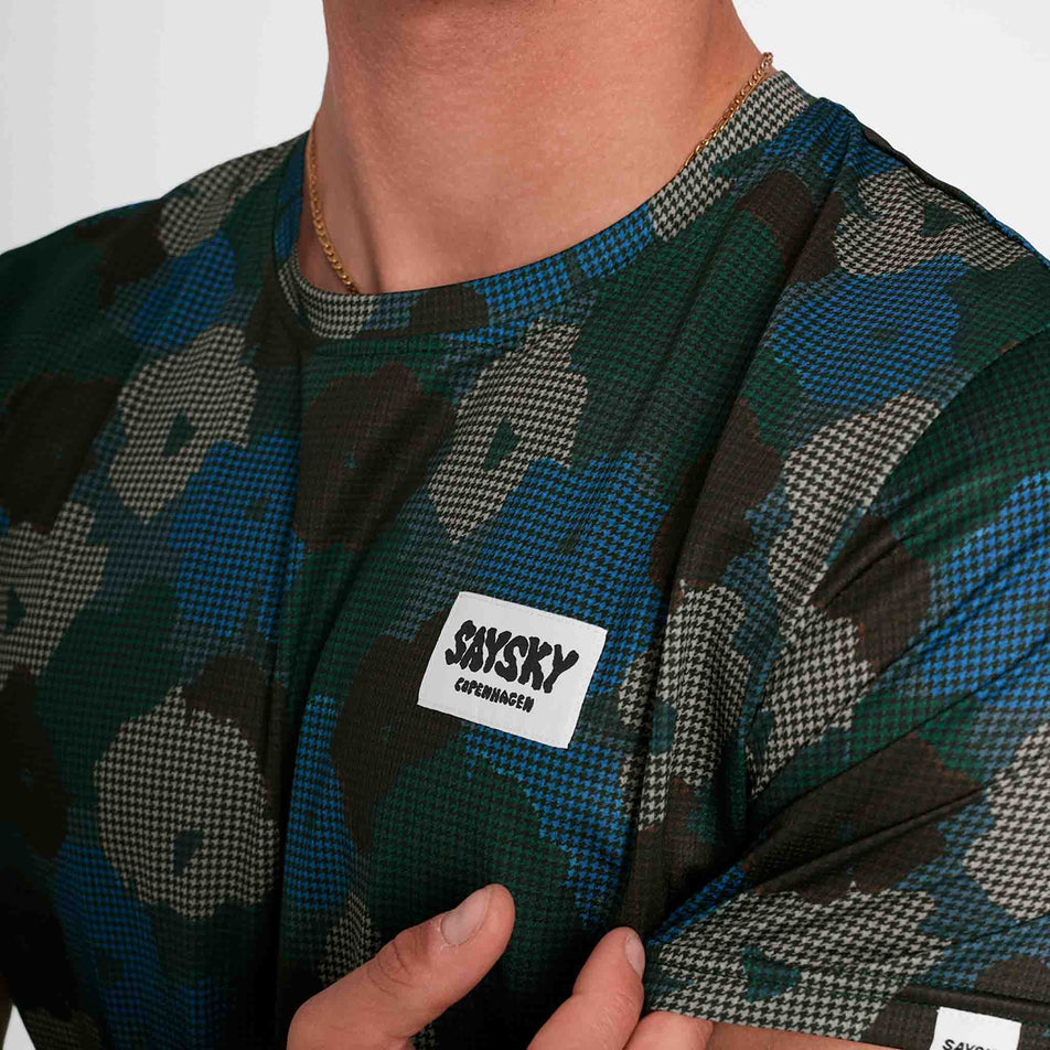 Close-up of the SAYSKY logo on the front of a SAYSKY Men's Flower Combat T-Shirt in the Blue AOP colourway. Top is being worn by a model. (8756181434530)