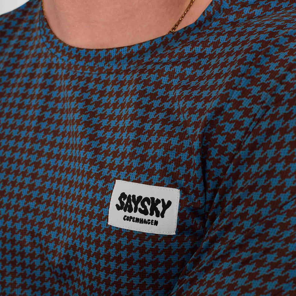 Close-up of the SAYSKY logo on the front of a SAYSKY Men's Houndstooth Combat T-Shirt in the Blue AOP colourway. Top is being worn by a model. (8756486439074)