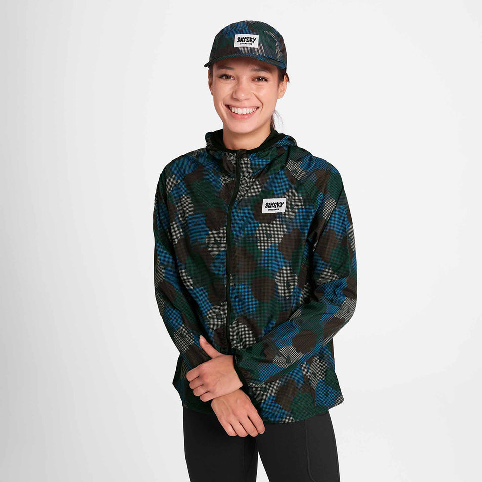 Front view of a model wearing the SAYSKY Women's Flower Pace Jacket in the Blue AOP colourway. Model is also wearing leggings and a cap. (8756501971106)