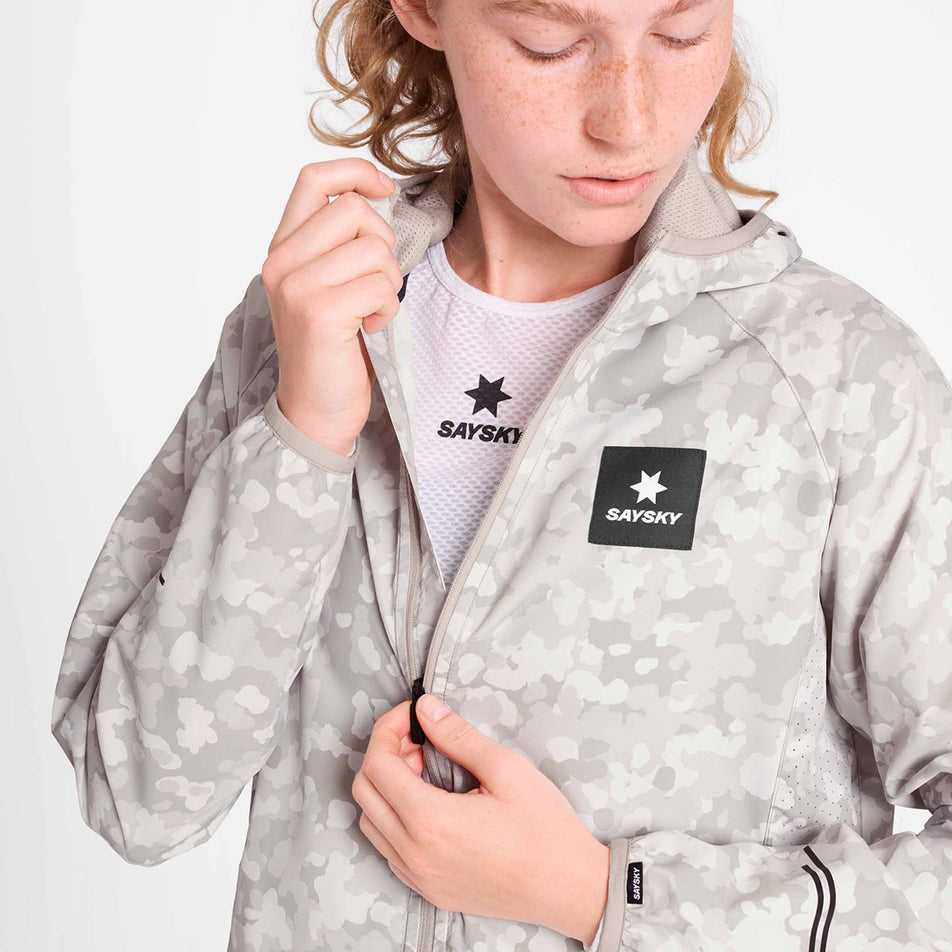 A model adjusting the zip on the SAYSKY Women's Camo Pace Jacket in the White colourway. (8781025869986)