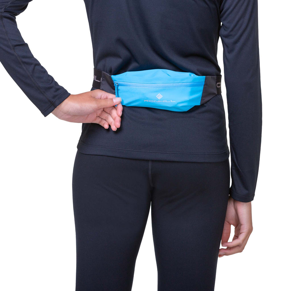 Close-up view of a model wearing a Ronhill Unisex Solo Waist Belt in the Cyan/Black colourway. Model is also wearing a long sleeve top and leggings. (8160945340578)
