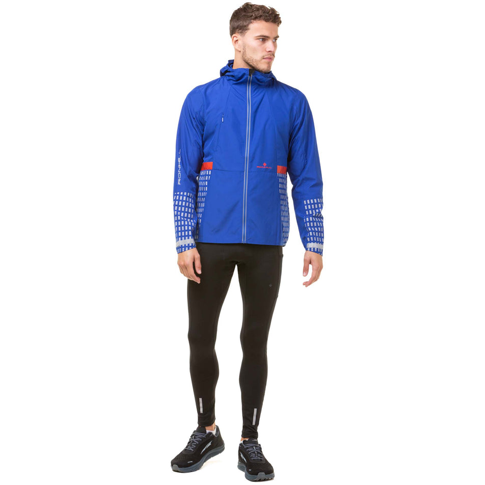 Front view of a model wearing a Ronhill Men's Tech Afterhours Jacket in the Cobalt/Flame/Reflect colourway. Model is also wearing black Ronhill running tights and black Altra running shoes.  (8032156385442)