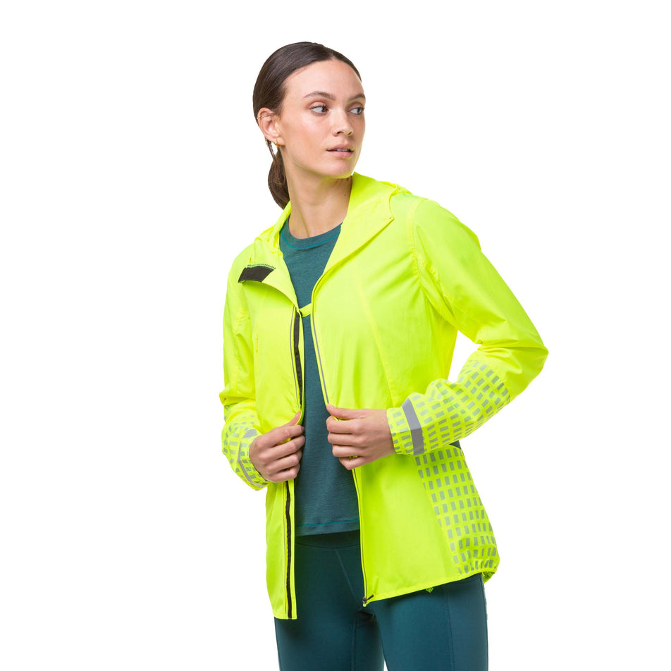 Front view of a model wearing a Ronhill Women's Tech Afterhours Jacket in the Fluo Yellow/Deep Lagoon/Reflect colourway. Jacket is unzipped, but the front sections are fastened together with a fastener at the chest. (8019130286242)