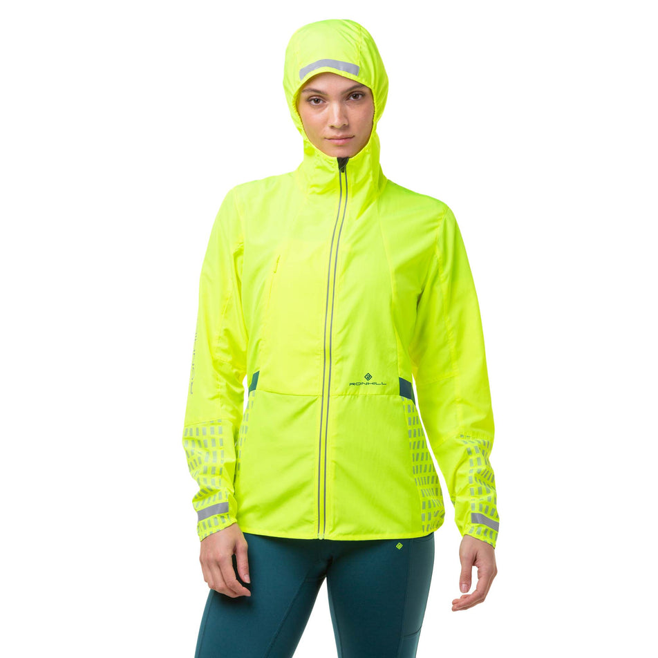 Front view of a model wearing a Ronhill Women's Tech Afterhours Jacket in the Fluo Yellow/Deep Lagoon/Reflect colourway. Jacket being worn with the hood up. (8019130286242)