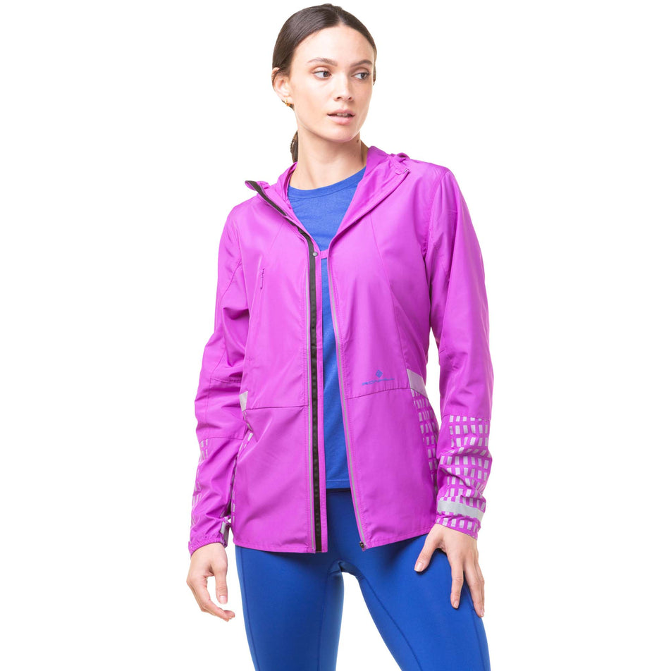 Front view of model wearing a Ronhill Women's Tech Afterhours Jacket in the Thistle/Cobalt/Reflect colourway. Jacket is unzipped, but the front sections are fastened together with a fastener at the chest. (8047250374818)