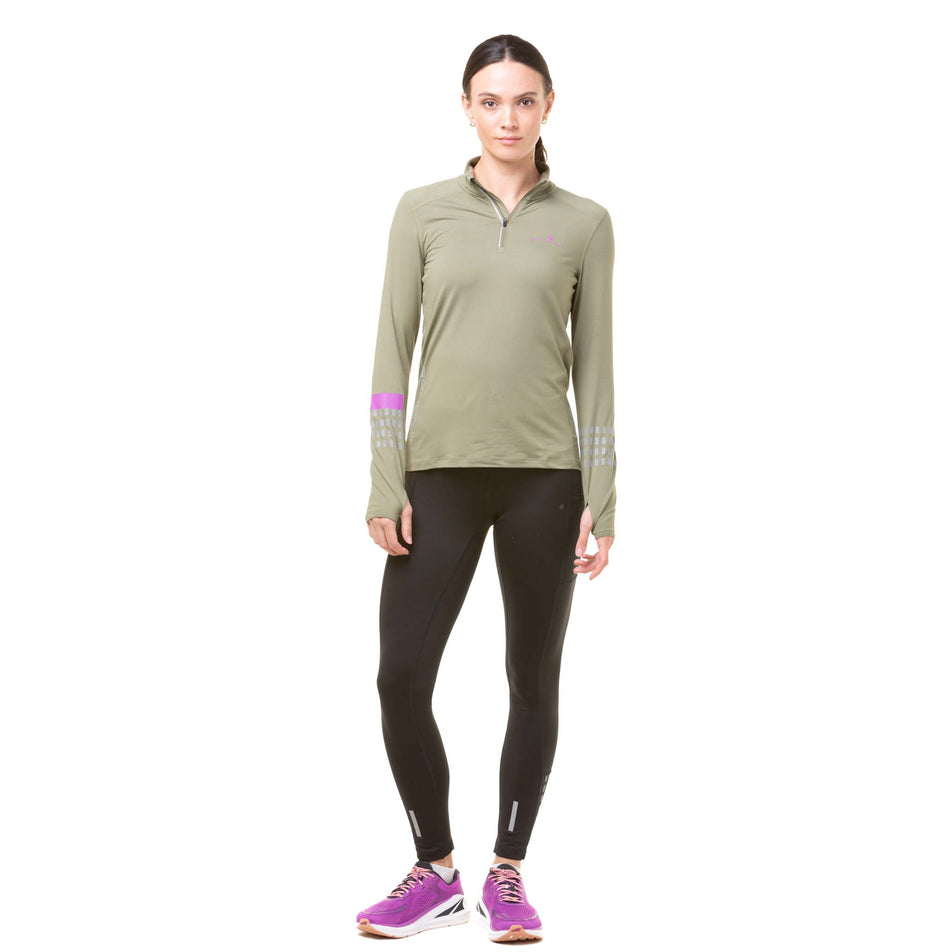 Front view of a model wearing a Ronhill Women's Tech Afterhours 1/2 Zip Tee in the Woodland/Thistle/Reflect colourway, and wearing a pair of black tights and pink trainers.  (8023190896802)