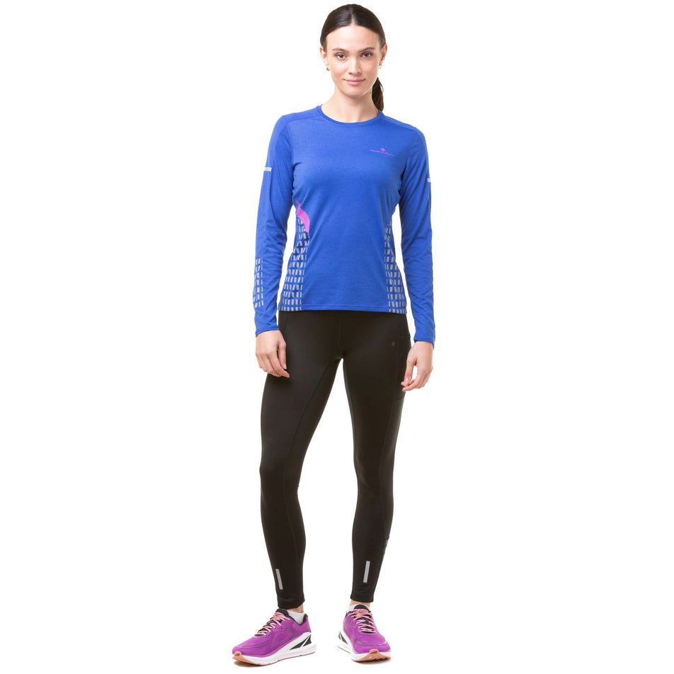 Front view of a model wearing a Ronhill Women's Tech Afterhours L/S Tee in the Cobalt/Thistle/Reflect colourway. Model is also wearing black Ronhill running leggings and purple Altra running shoes. (8047287500962)