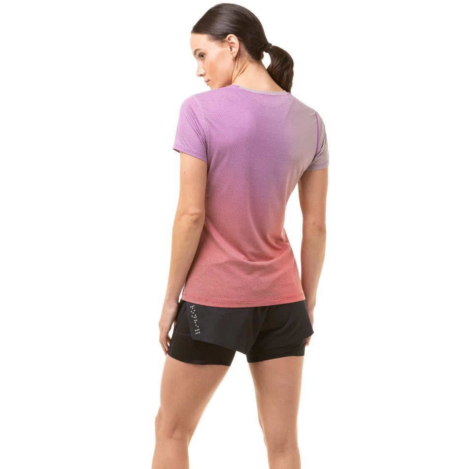 Back view of a model wearing a Ronhill Women's Tech Goldenhour Tee in the Jam/Stardust Merge colourway. Model is also wearing black Ronhill running shorts. (8031399248034)