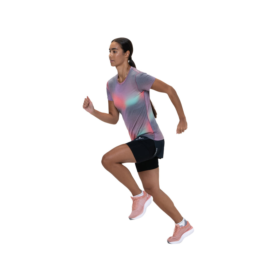Angled view of a model wearing the Ronhill Women's Tech Golden Hour Tee in the Multi Glow colourway. (8742692126882)