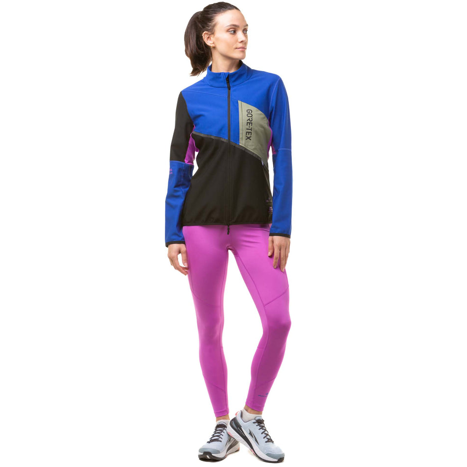 Front view of a model wearing a Ronhill Women's Tech Gore-Tex Windstopper Jacket in the Black/Cobalt colourway. Model is also wearing a Ronhill running leggings and Altra running shoes. (8024339841186)