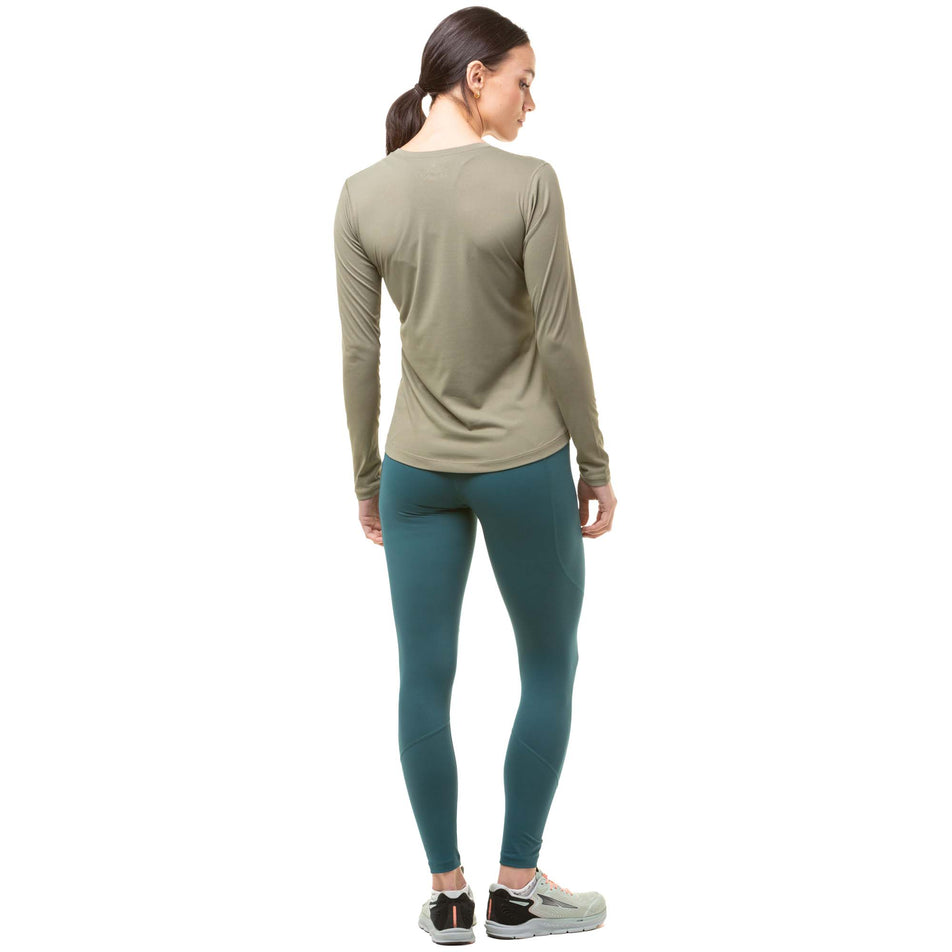 Back view of a model wearing a pair of Ronhill Women's Tech Tights in the Deep Lagoon/Copper colourway. Model also wearing a green Ronhill long sleeve top and grey Altra running shoes. (8024370315426)